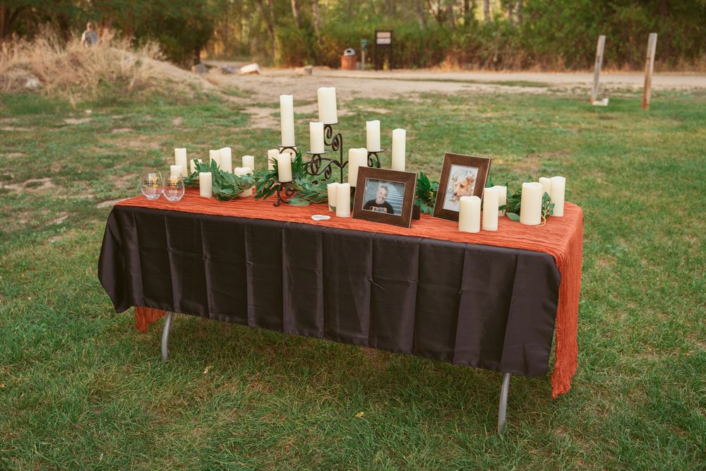 A memorial table decorated with candles and photographs on a red tablecloth outdoors.