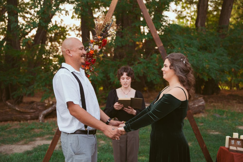 An outdoor wedding ceremony taking place under trees with autumn decorations.