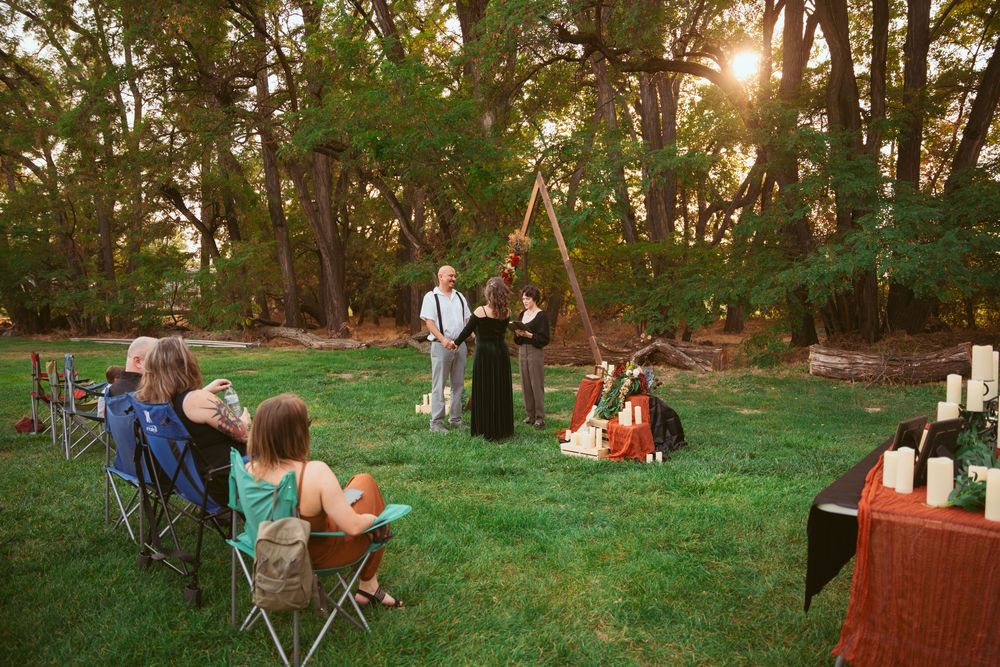 An intimate outdoor wedding ceremony in a park with guests seated on lawn chairs at sunset.