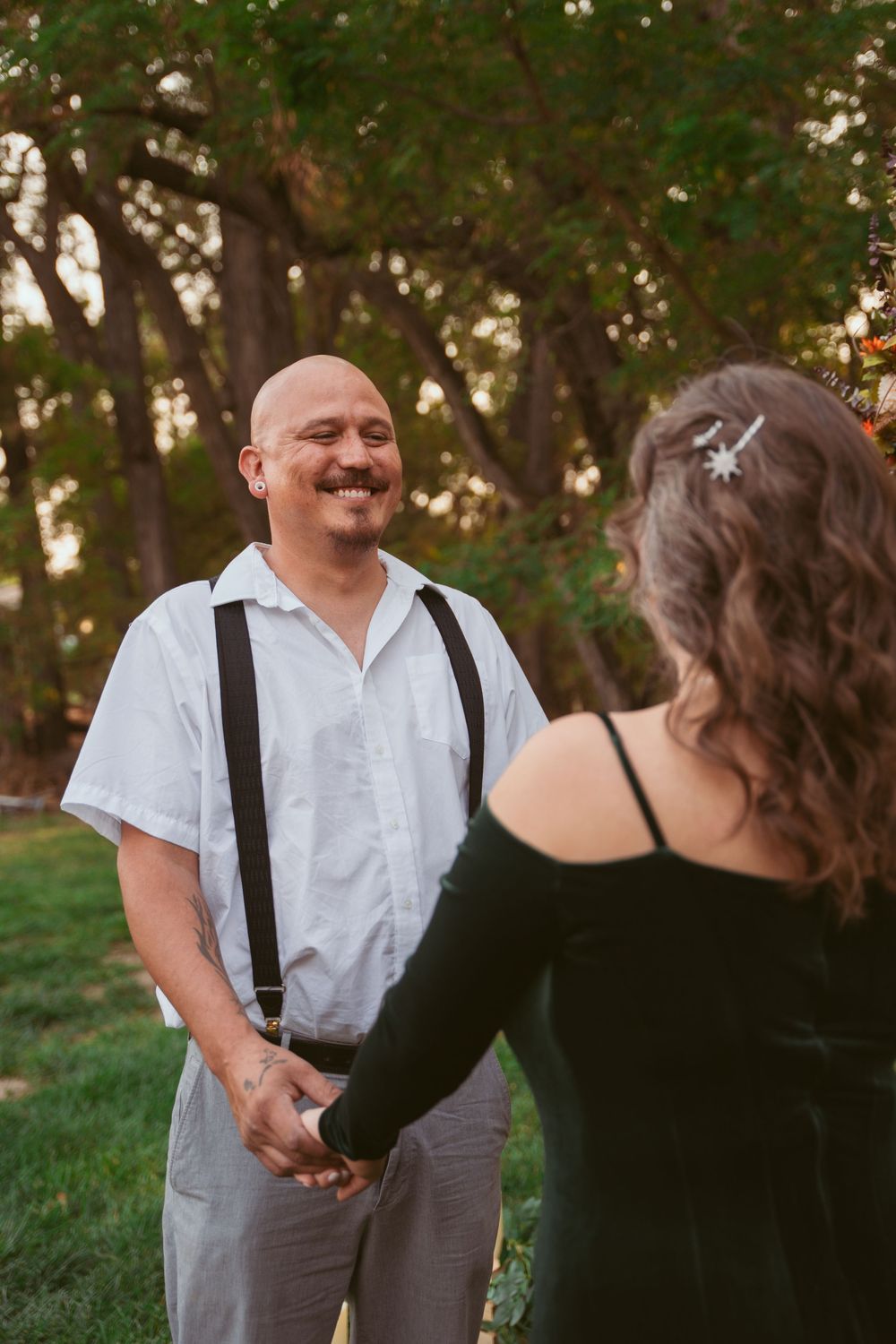 A couple shares a joyful moment together in a sunny outdoor setting with green trees in the background.