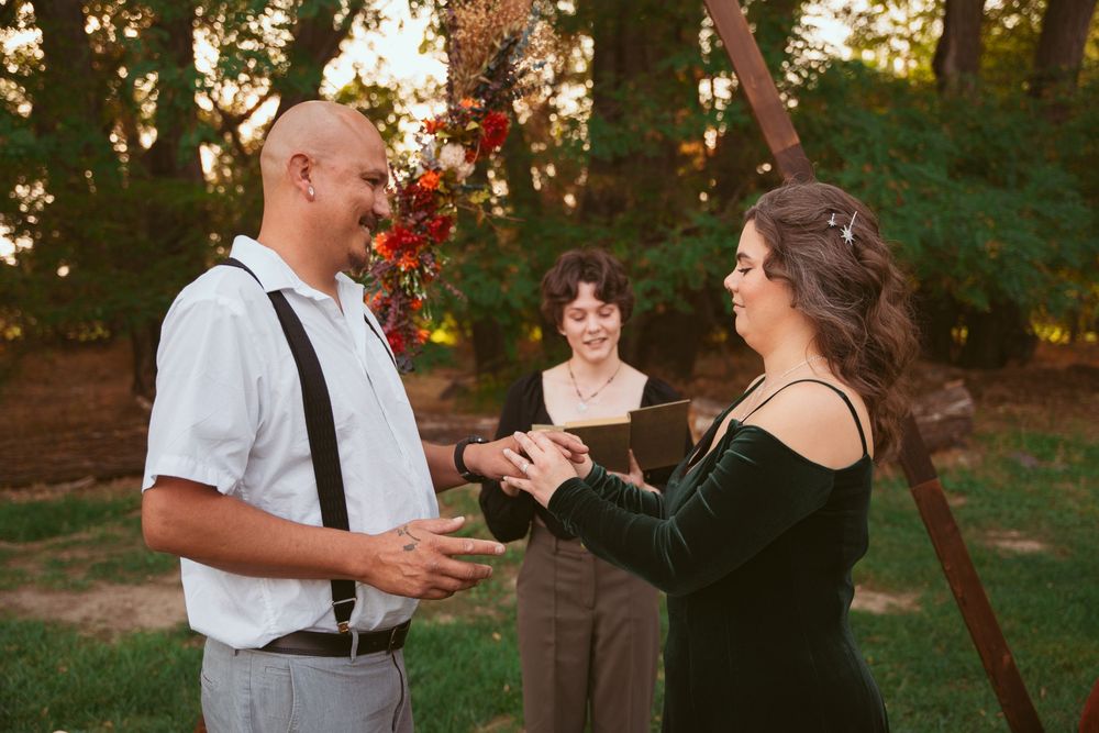 A couple exchanging vows under a floral arch during an outdoor ceremony.