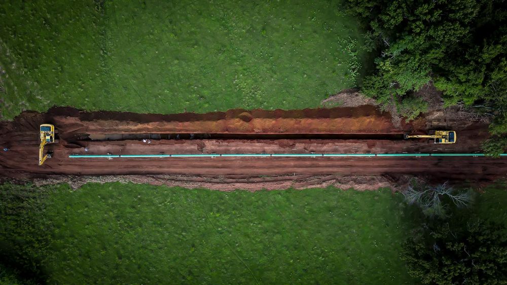 Aerial view of pipeline construction through green field.
