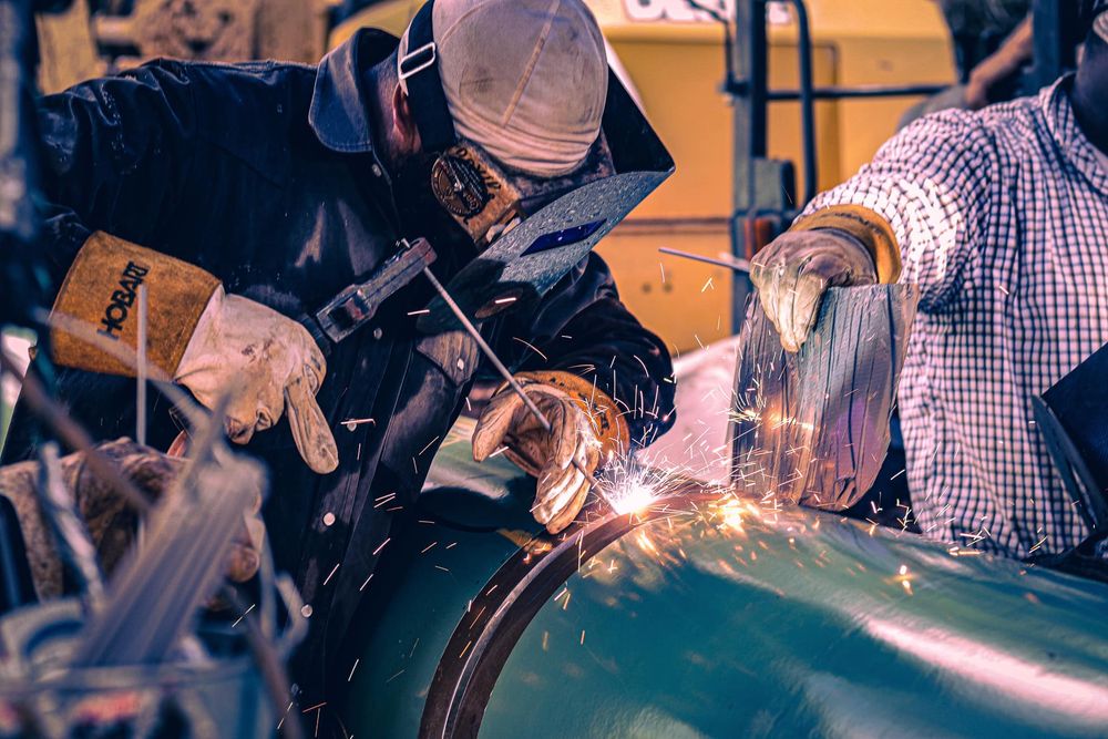Welder working on metal pipe with sparks flying during construction.