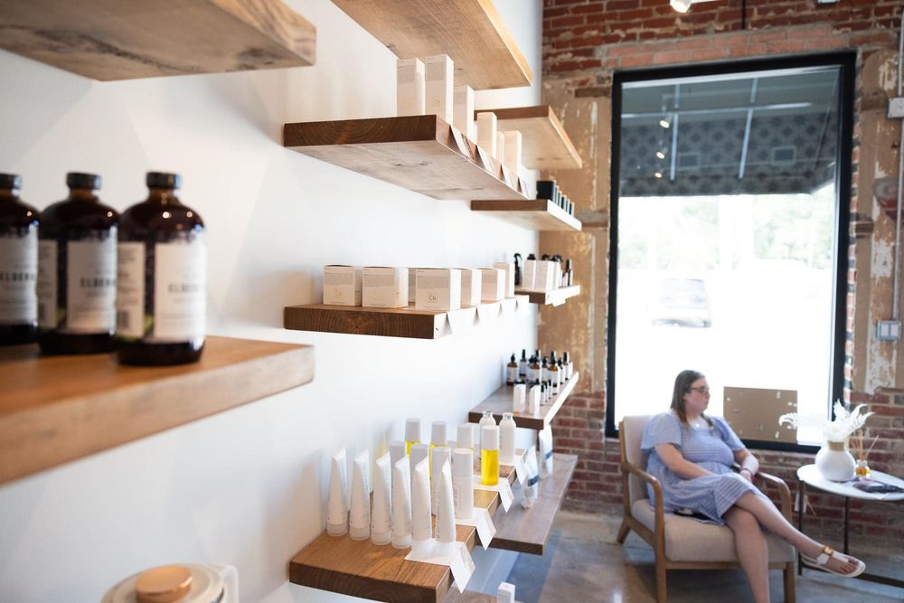 Wooden shelves displaying amber glass bottles and products in a rustic retail space with exposed brick walls.
