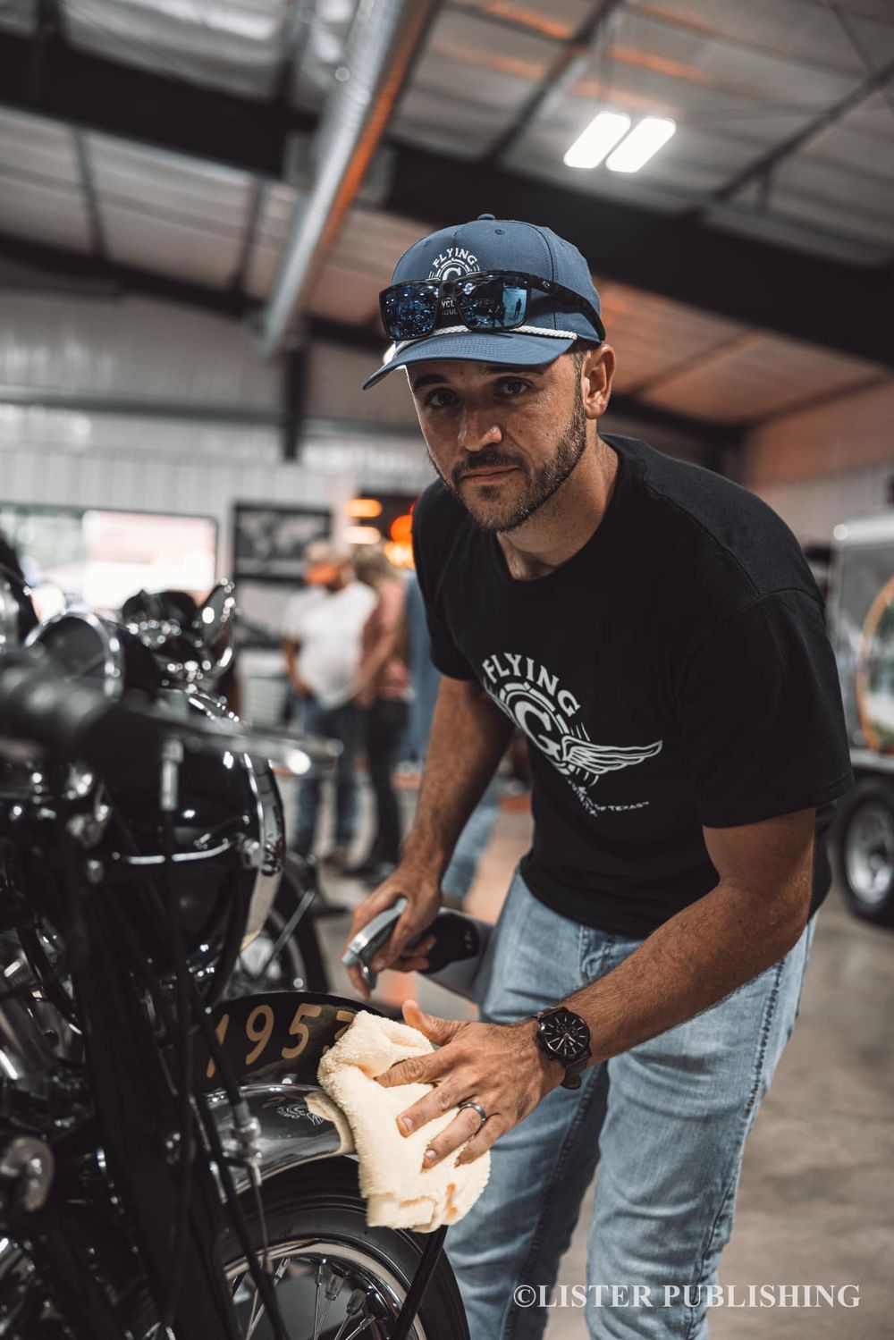 Person in baseball cap working on vintage motorcycle in industrial workspace.