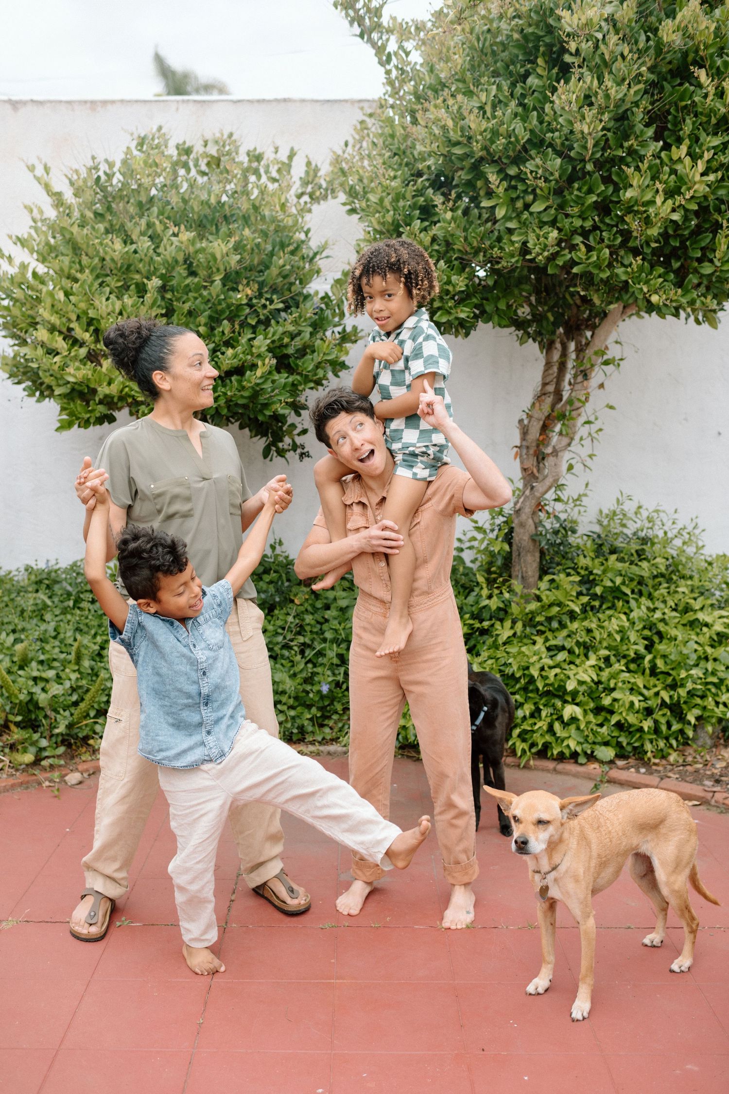 Playful sequence of two people and a golden dog posing energetically on a terracotta patio near garden shrubs.