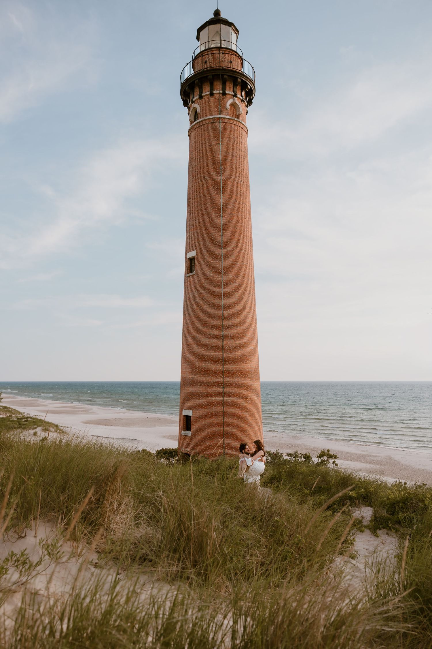 Tall brick lighthouse stands majestically on sandy dunes overlooking the beach and ocean on a cloudy day. Rachel Martinez Photography