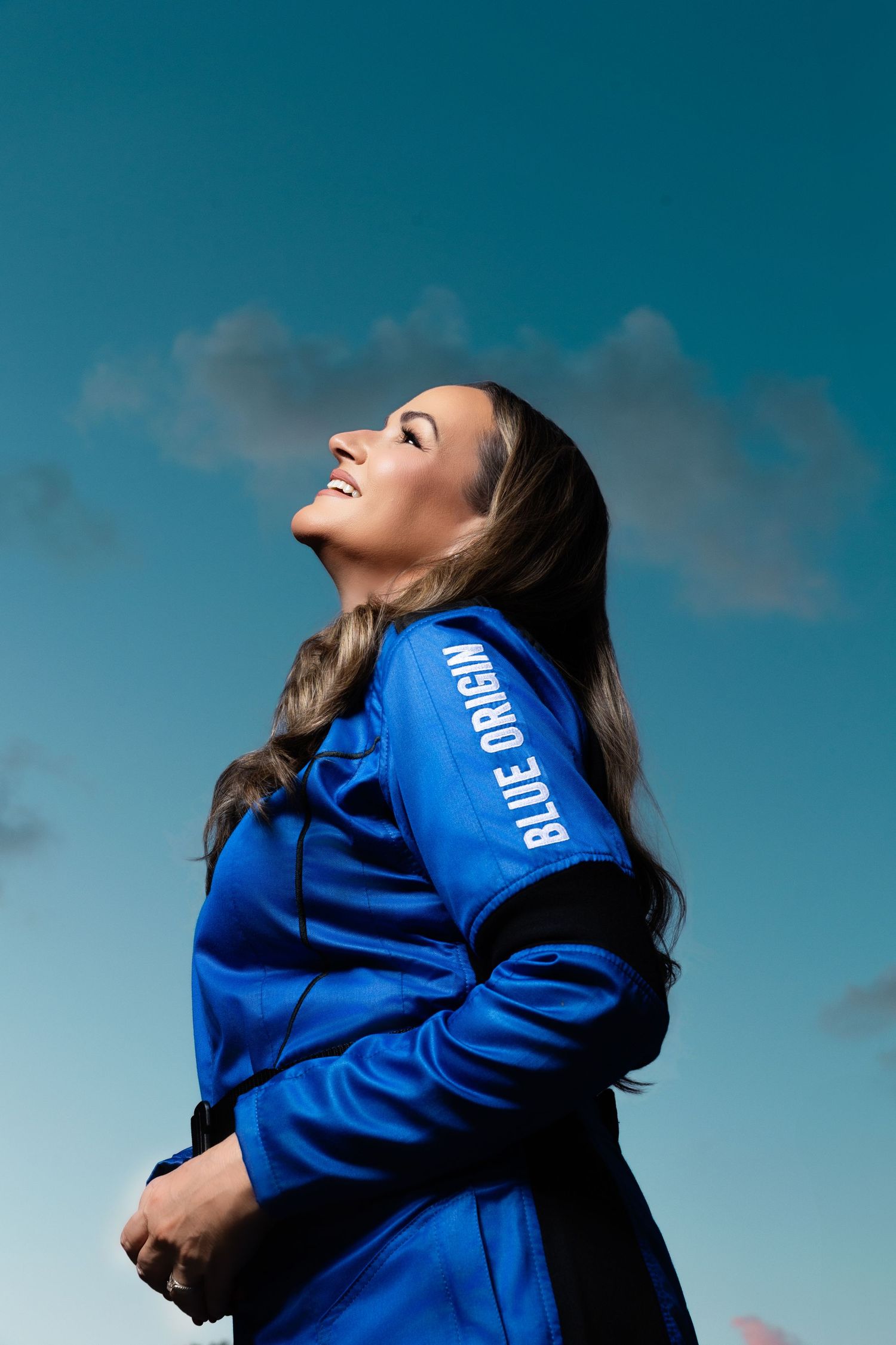 Athletic figure in blue hoodie set against dramatic sky background creating dynamic outdoor fashion portrait.