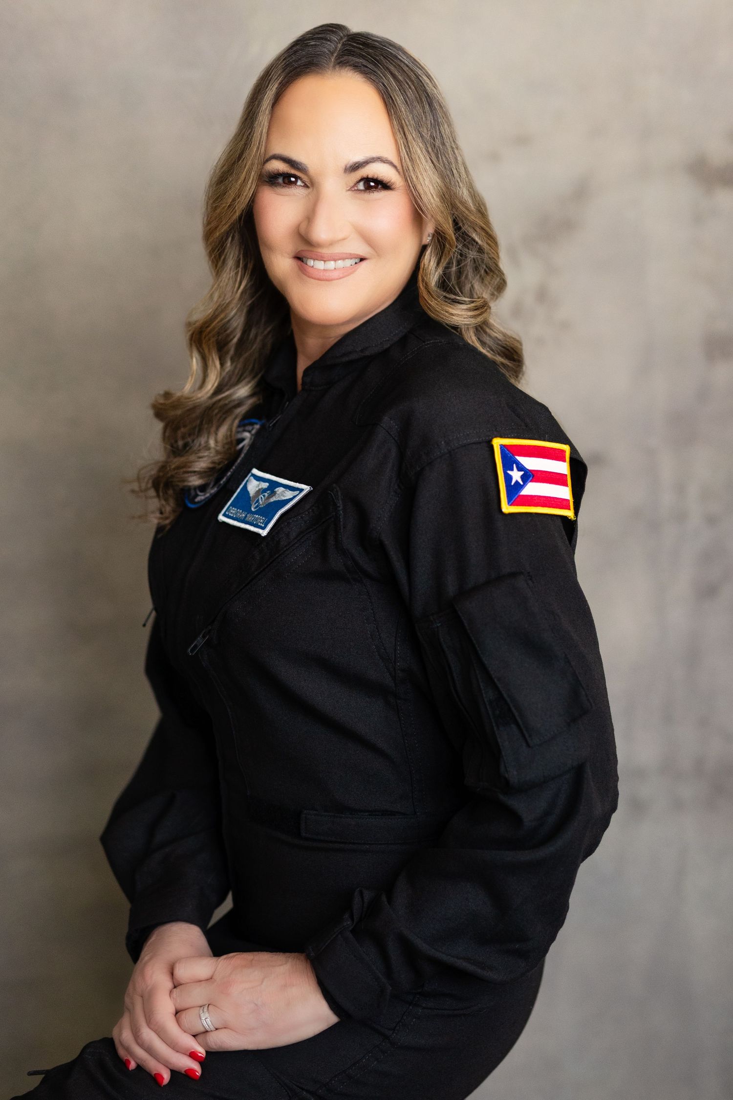 Professional headshot photos of someone in a black jacket with flag patches posing against a textured gray background.