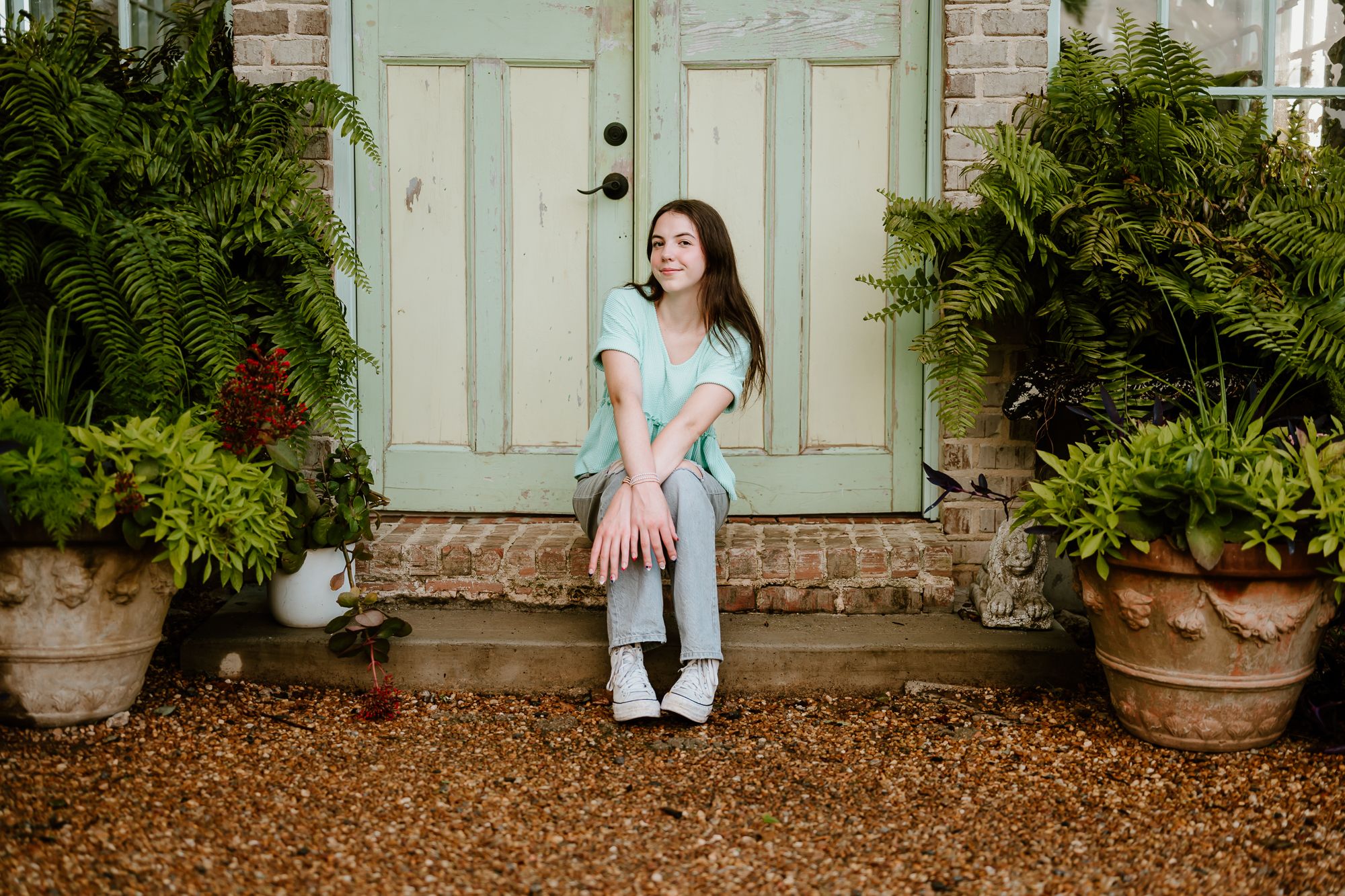 A person in a pink flowy dress sits delicately against a rustic white door with vintage charm.