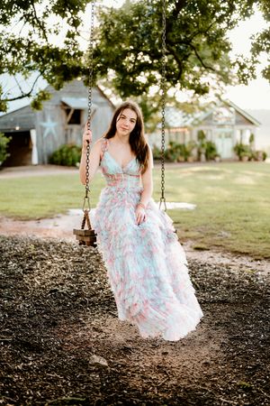 Someone wearing a floral blue and pink dress sits on an old wooden swing in a backyard setting.