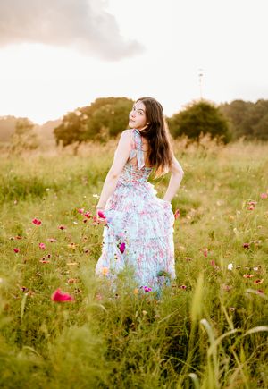 A person in a flowing floral dress walks through a wildflower meadow during golden hour.