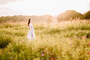 A dreamy summer scene shows a figure in a flowy dress standing among wildflowers in a golden-lit field.