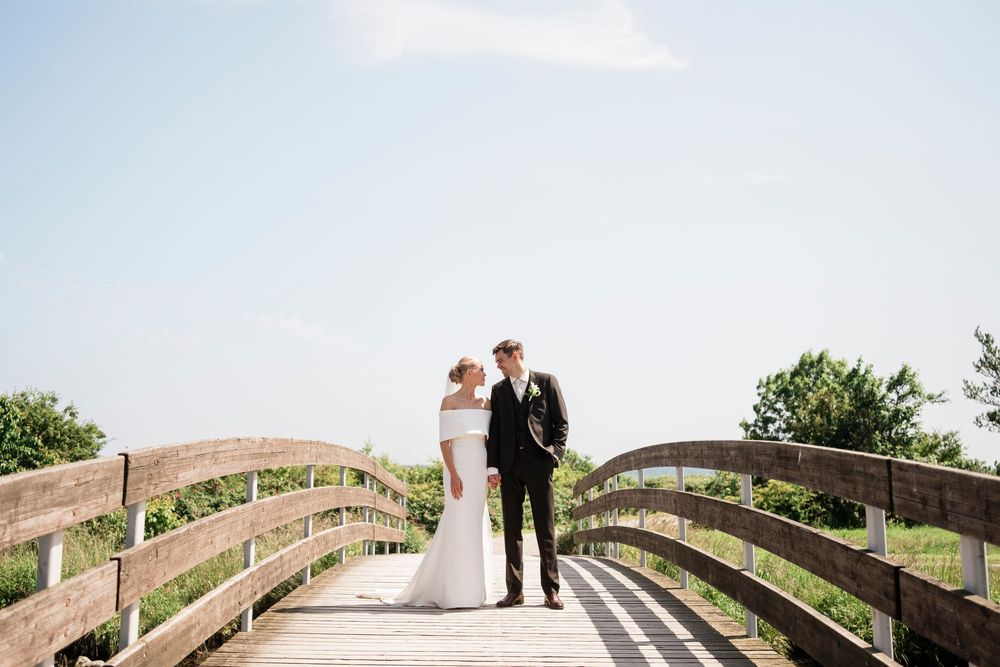 Wedding couple poses on rustic wooden bridge walkway in serene outdoor garden setting.