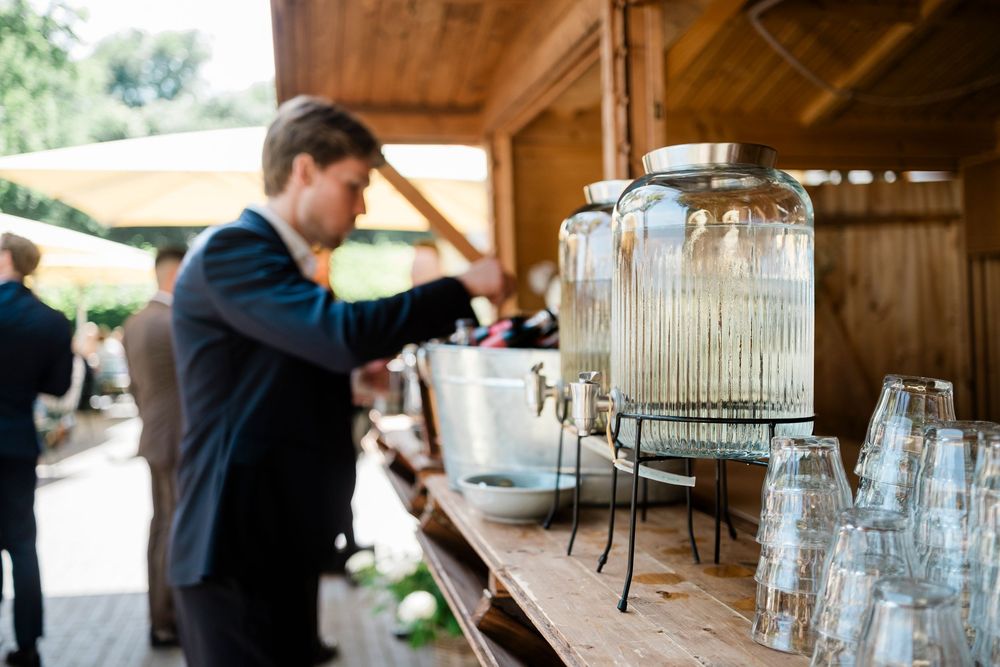 A rustic wooden drink station setup with glass beverage dispensers and clear glassware on display at an outdoor venue.