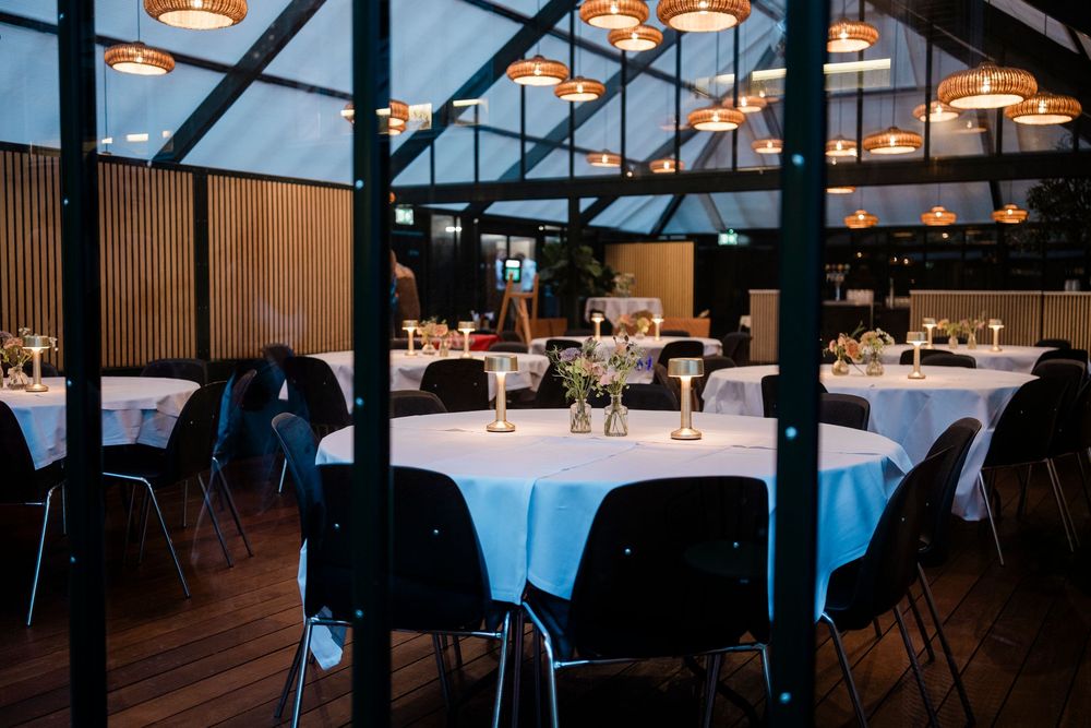 Elegant industrial restaurant space with pendant lighting and dark wood floors overlooking city views at dusk.