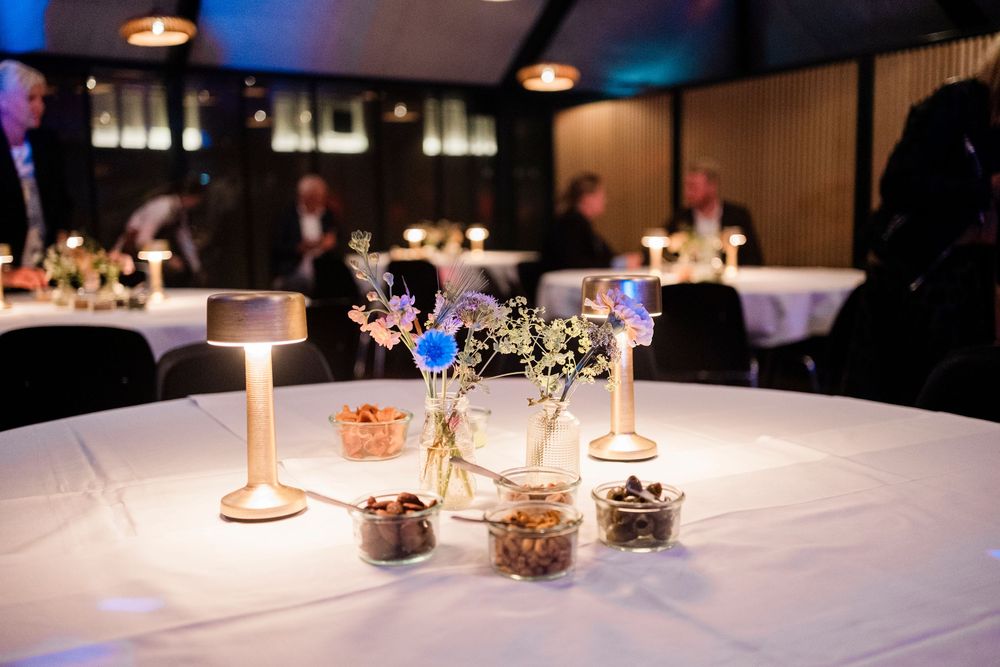 Elegant table setting with white linens, glass vases with flowers, and candlelight at an indoor evening reception.