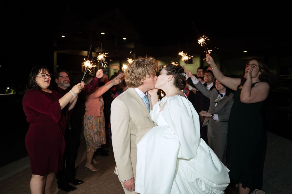 Wedding guests hold sparklers during a nighttime send-off celebration.