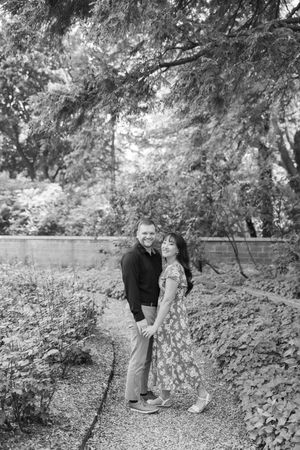 A couple shares a romantic moment walking together along a tree-lined path in black and white photography.