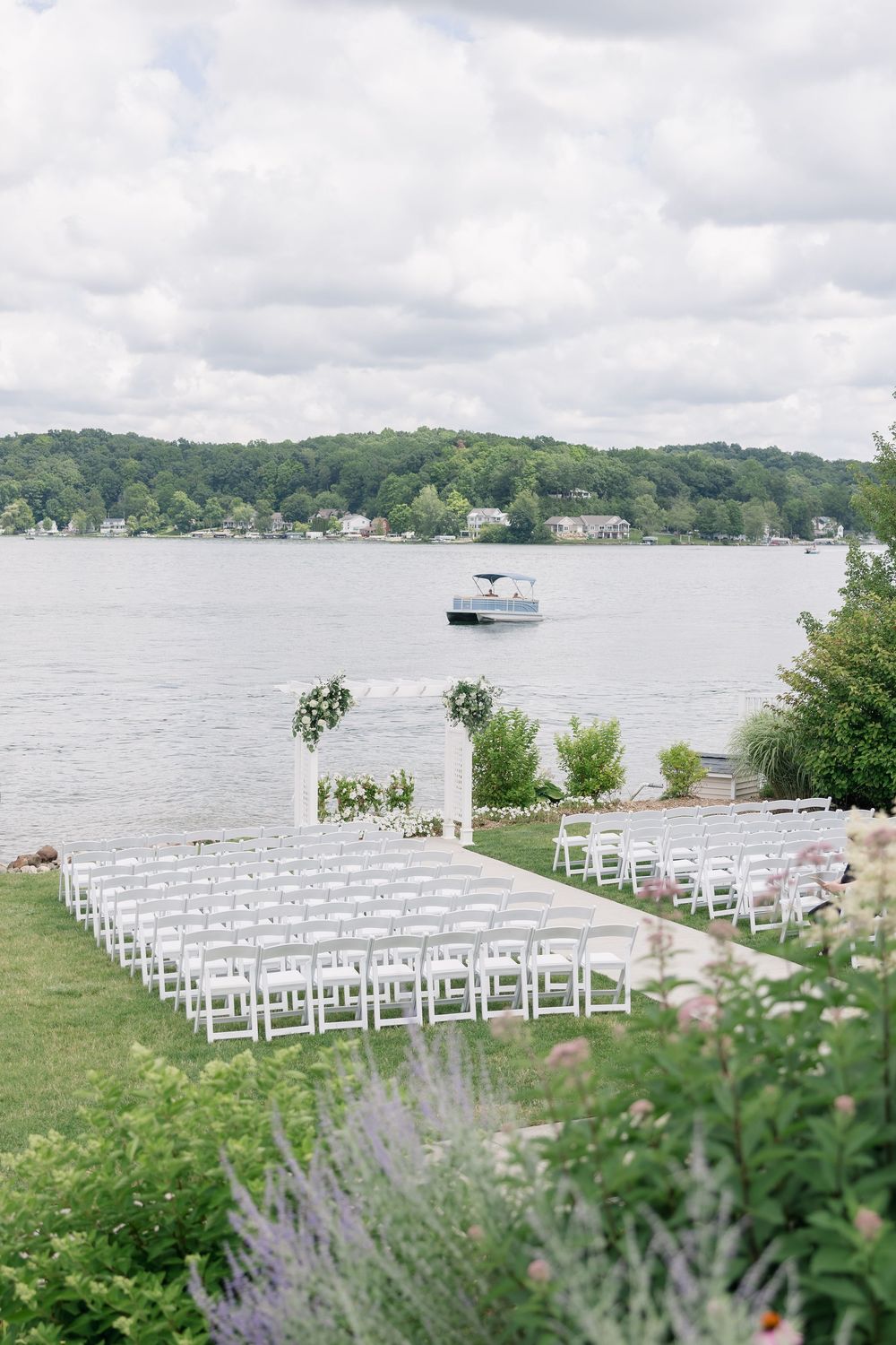 White chairs arranged in rows for a waterfront wedding ceremony with a scenic lake and lush green hills in the background.