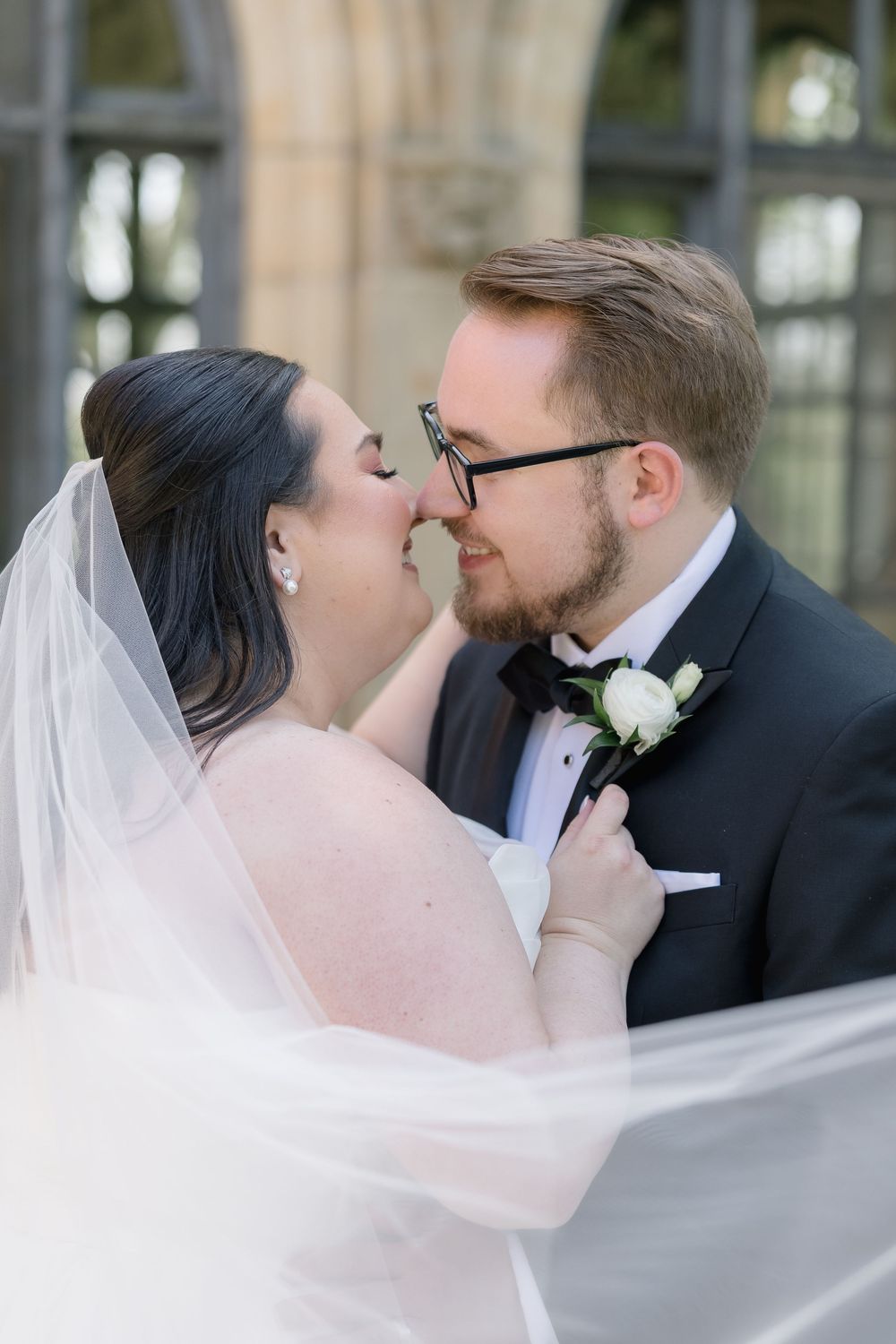 A newly married couple shares an intimate moment as the bride's veil flows in the breeze on their wedding day.