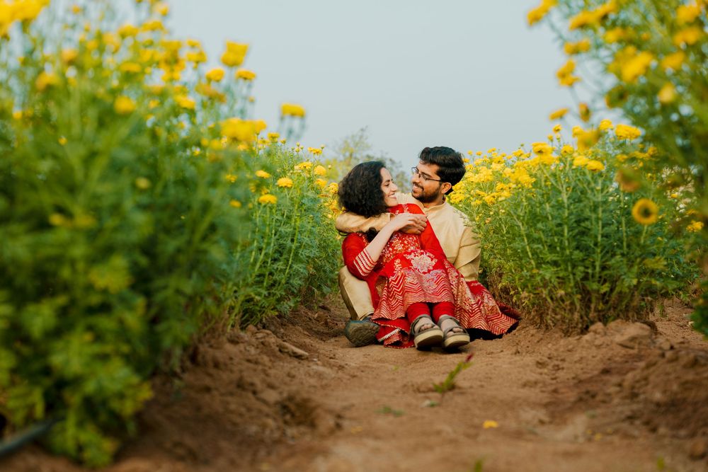A couple in traditional Indian attire posing together in a blooming yellow sunflower field.