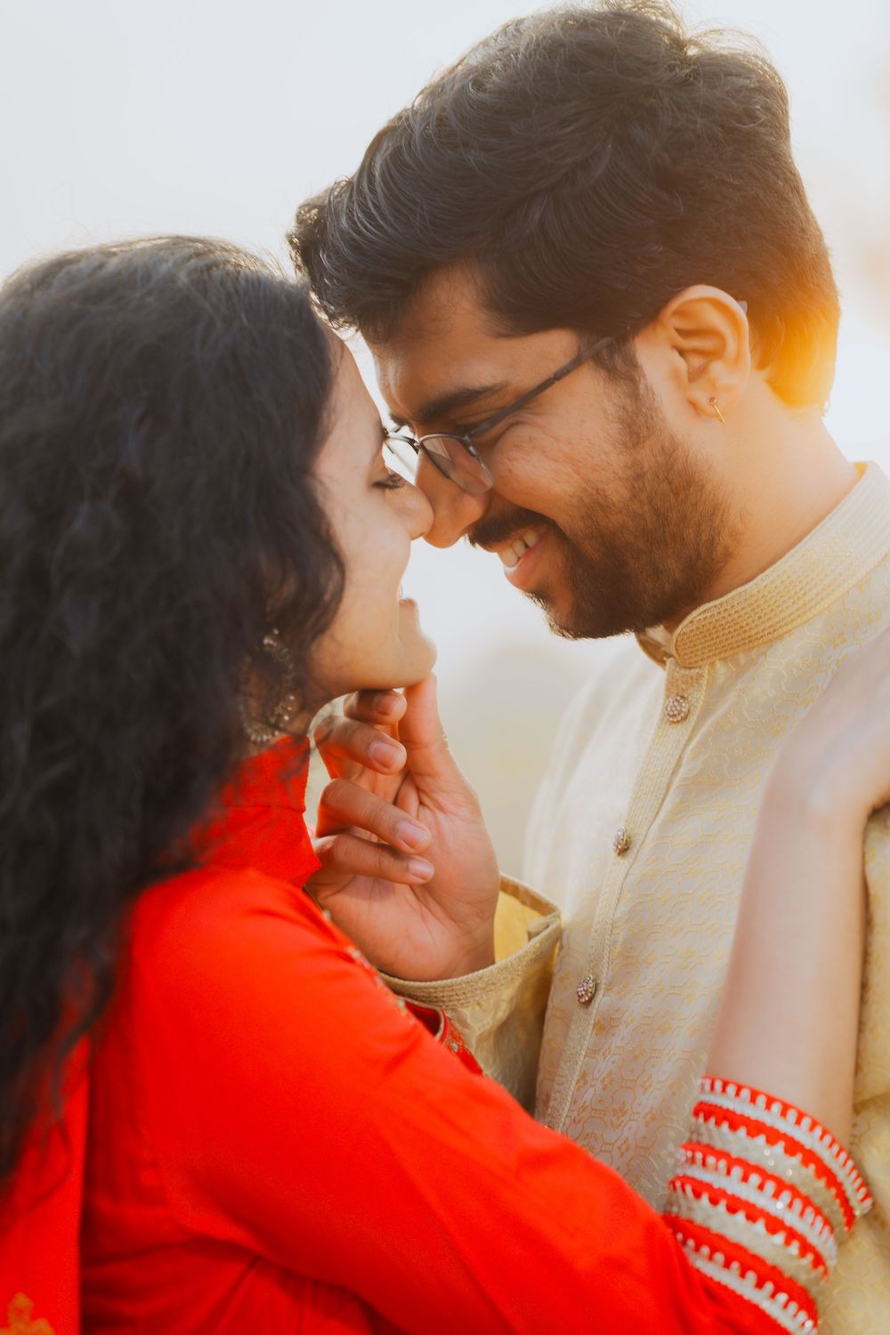 A romantic couple shares an intimate moment in warm sunlight while wearing traditional South Asian attire.