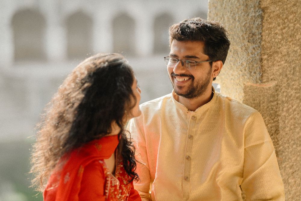 A couple in traditional Indian attire share a tender moment against an architectural backdrop.