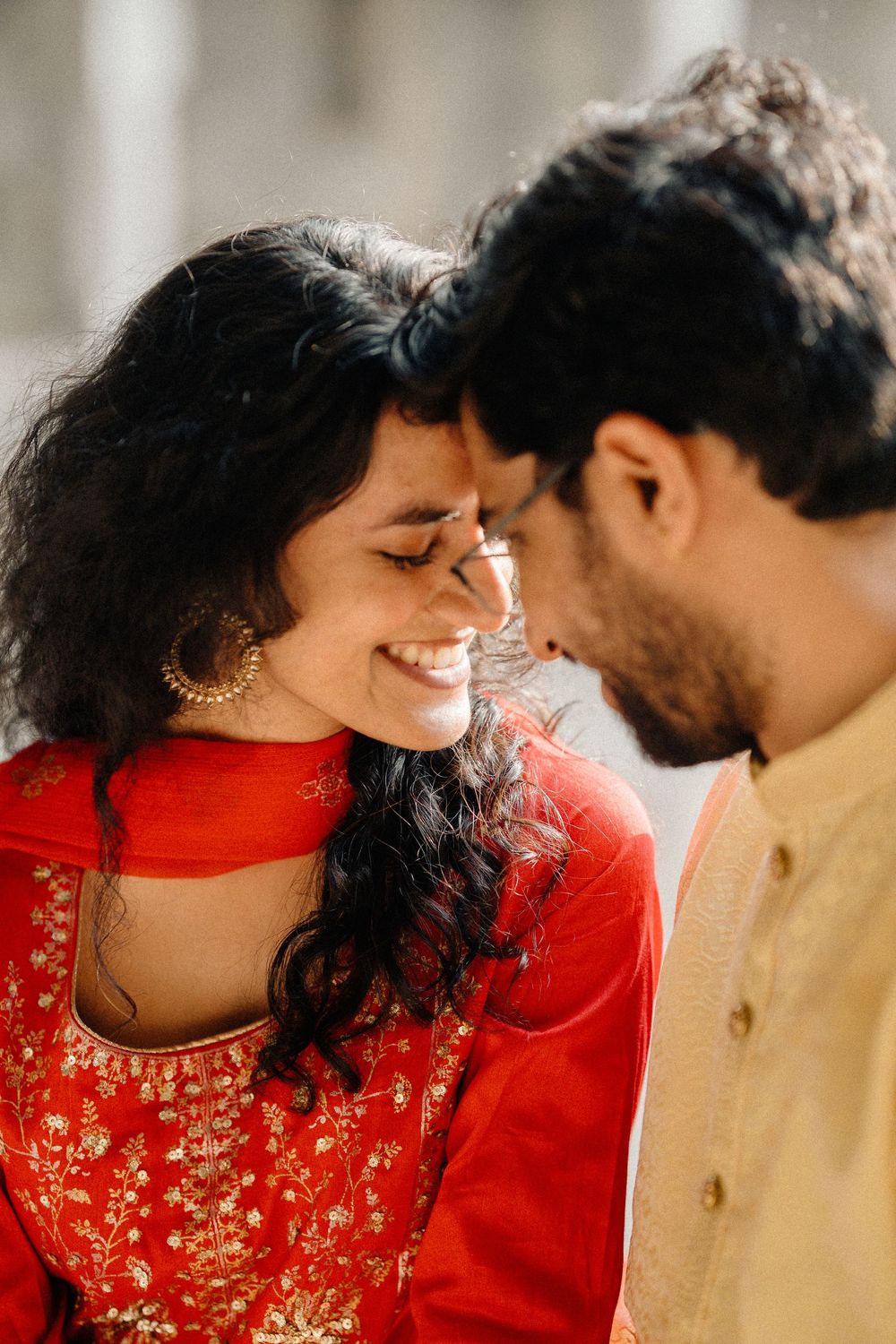 A couple in traditional South Asian attire sharing an intimate moment, with the woman wearing a vibrant red outfit.