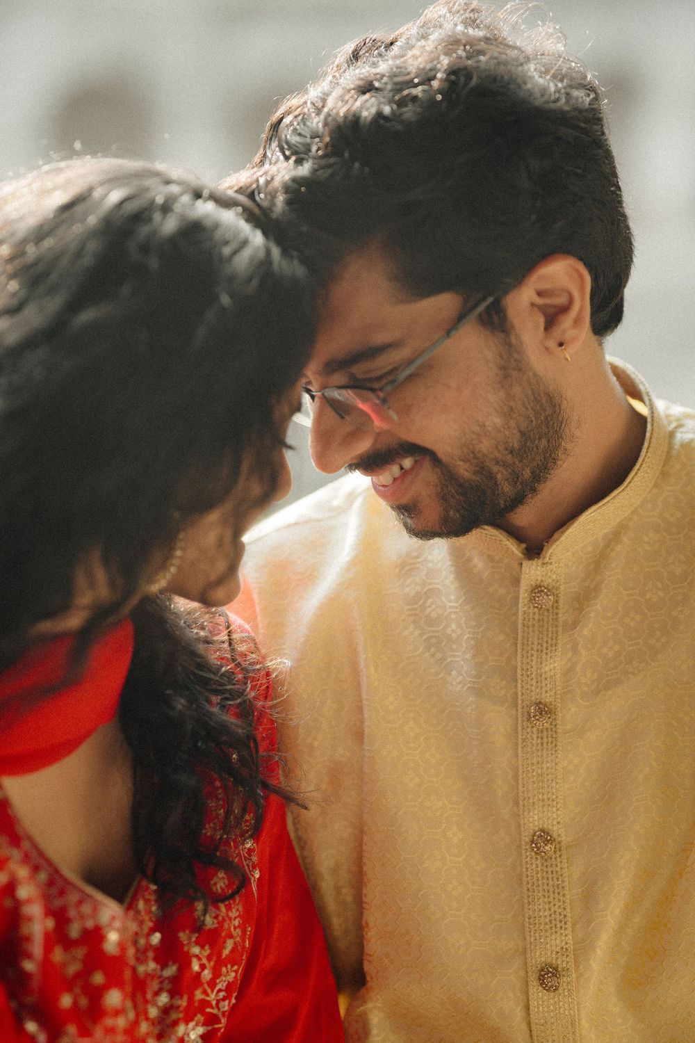 A couple share an intimate moment while dressed in traditional South Asian attire, the woman in red and man in beige.