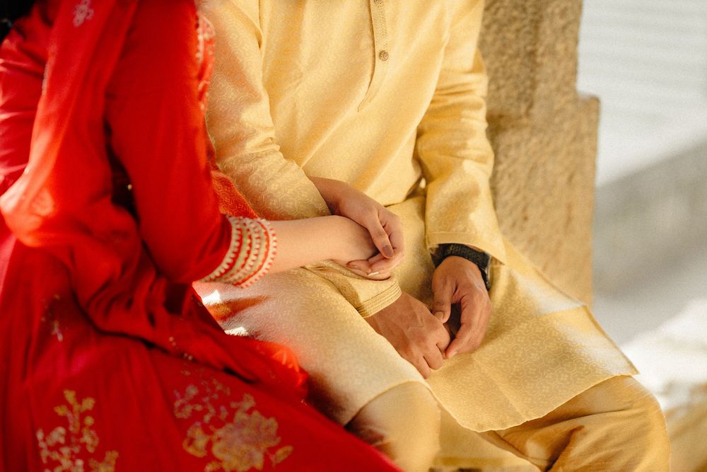 Close up of hands in traditional Indian wedding attire with red and gold garments holding together.