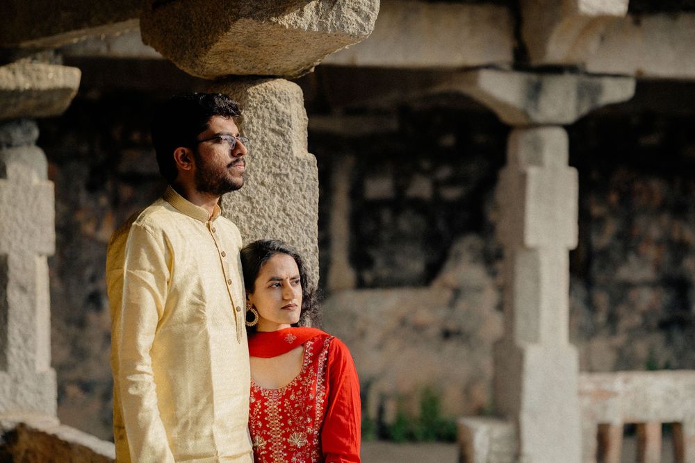 A couple in traditional Indian attire poses against ancient stone pillars and architecture.