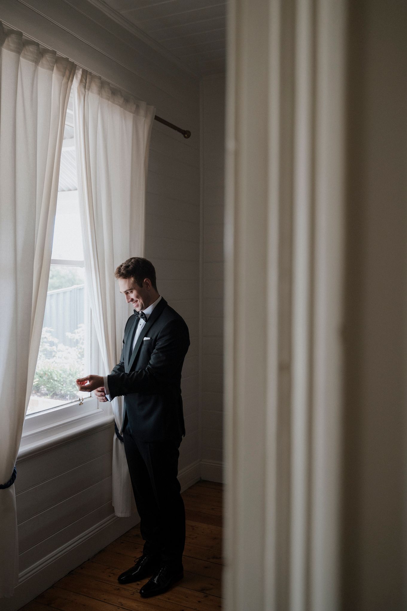 Side view of person in tuxedo looking out window in elegant room.