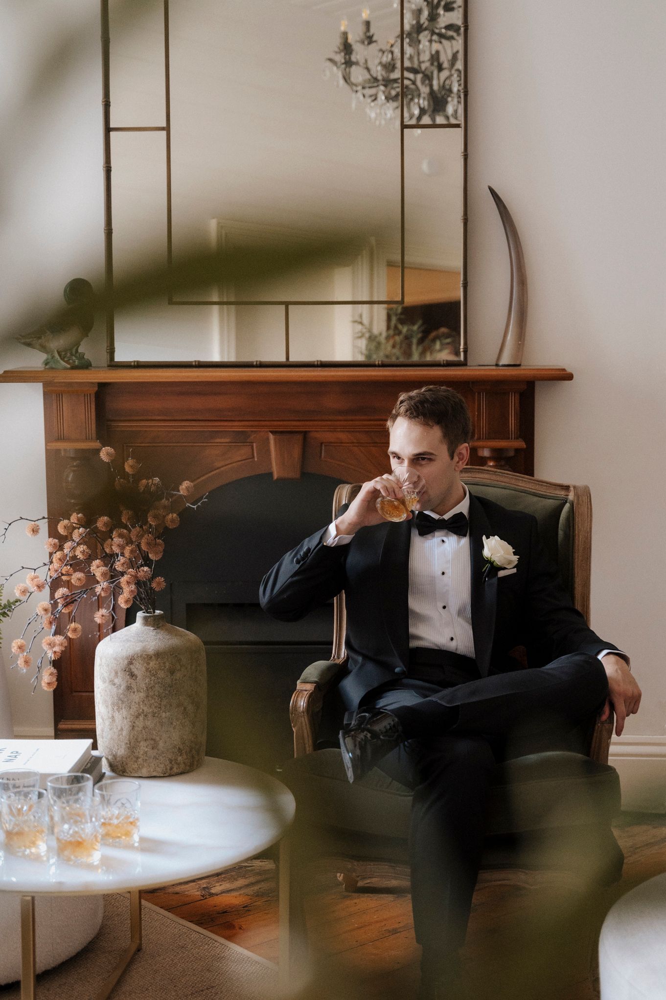 Person in tuxedo relaxing with drink in elegantly furnished room.