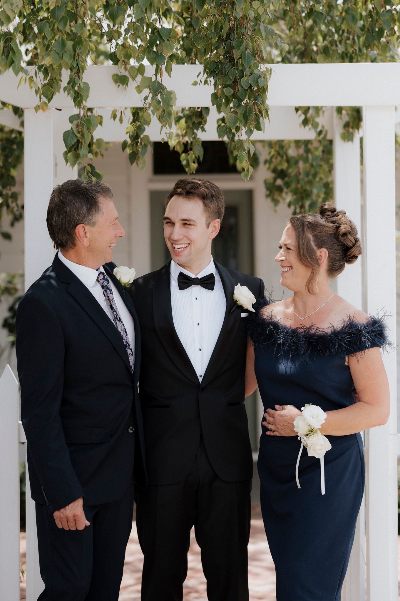 A formal wedding portrait under a white archway with hanging branches.
