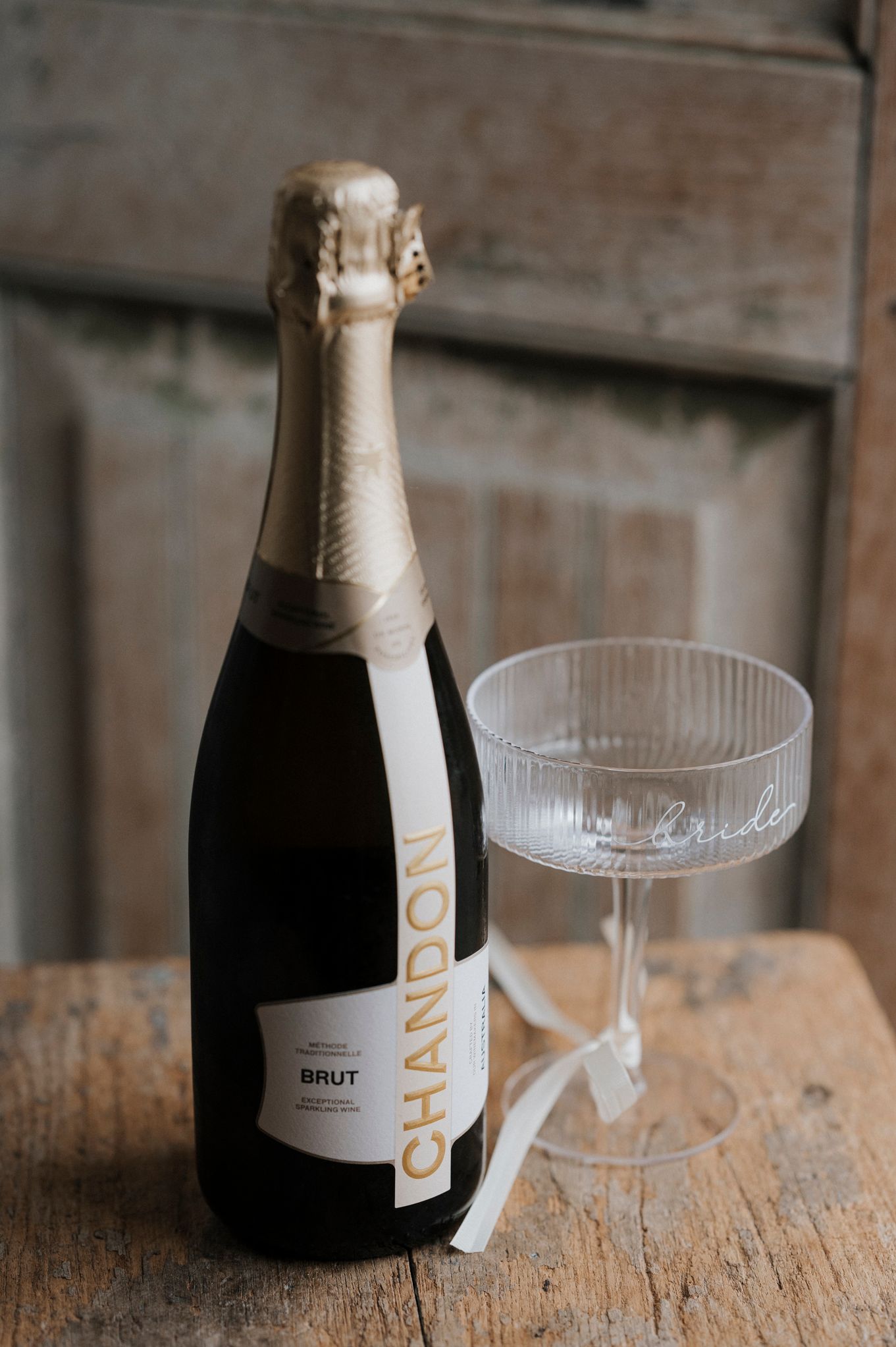 A bottle of champagne and crystal coupe glass arranged on a rustic wooden surface.