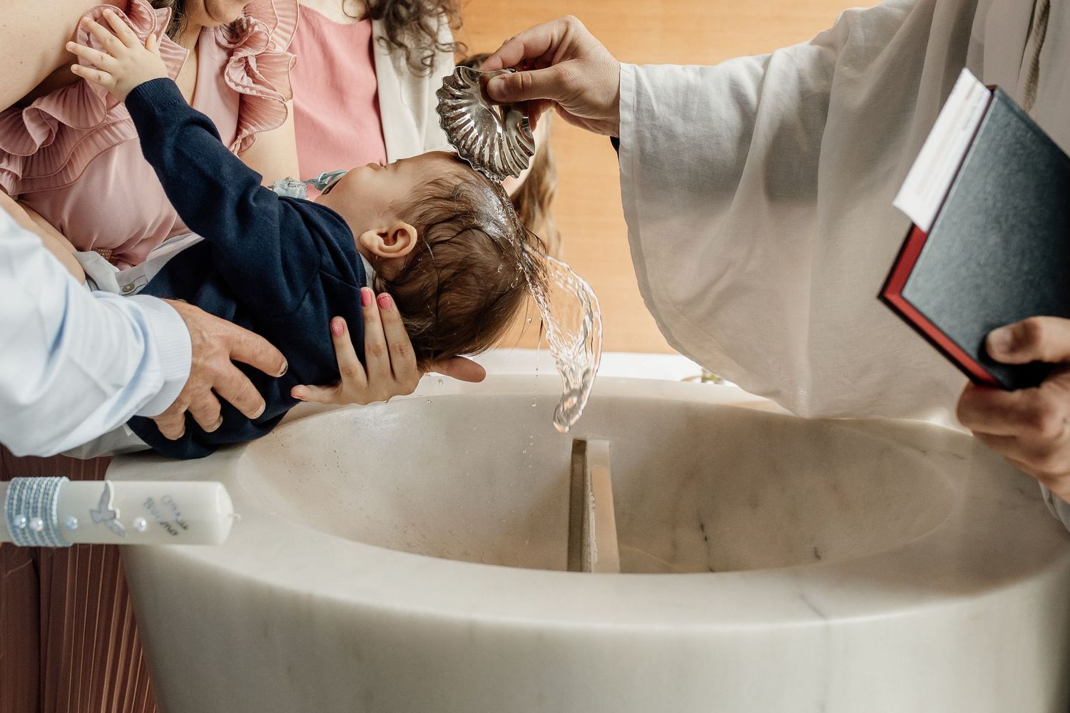 A person being baptized in a white baptismal font while clergy members in white robes assist during the religious ceremony.