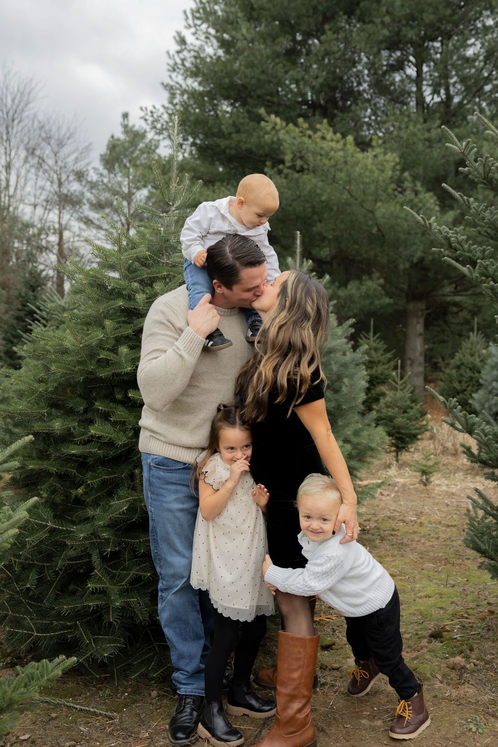 A family shares tender moments and embraces while standing among evergreen trees in a natural outdoor setting in Oakland county michigan