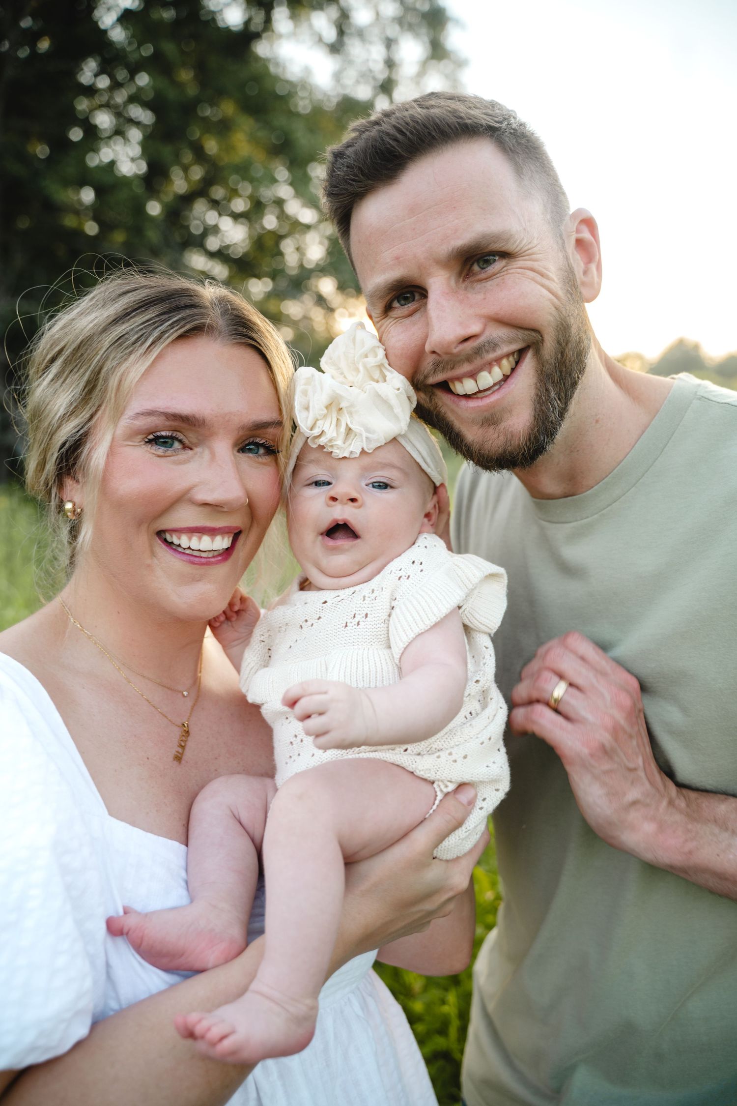 Happy family of three laughs together during outdoor summer photoshoot.