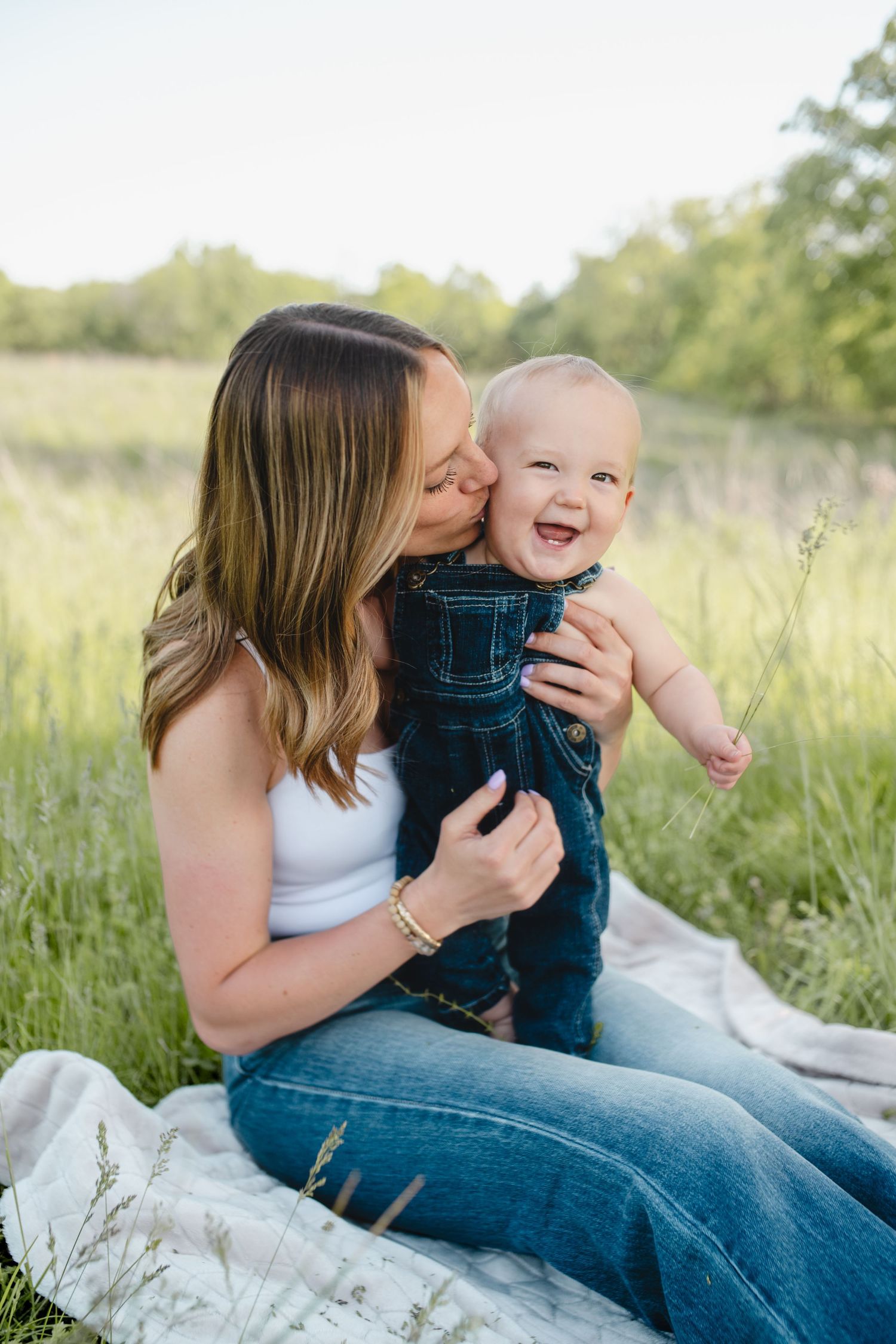 Mother and baby sharing joyful moments together on a blanket in a sunny field.