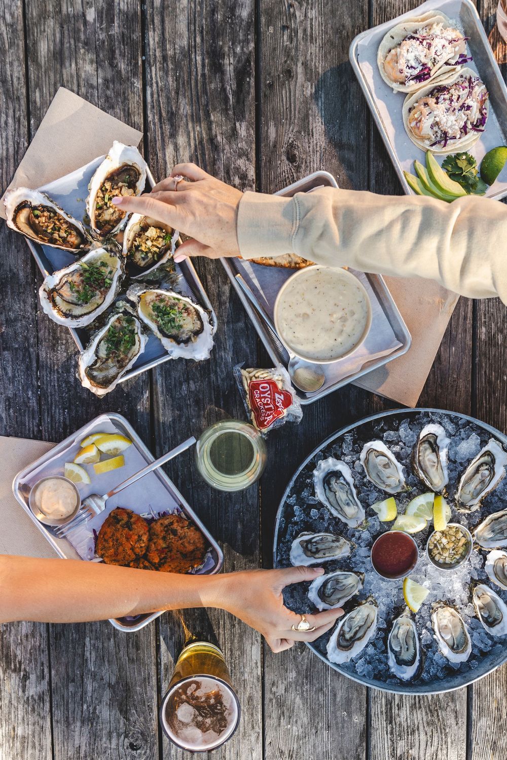 Overhead view of fresh oysters on ice with various sauces and condiments served on a rustic wooden table.