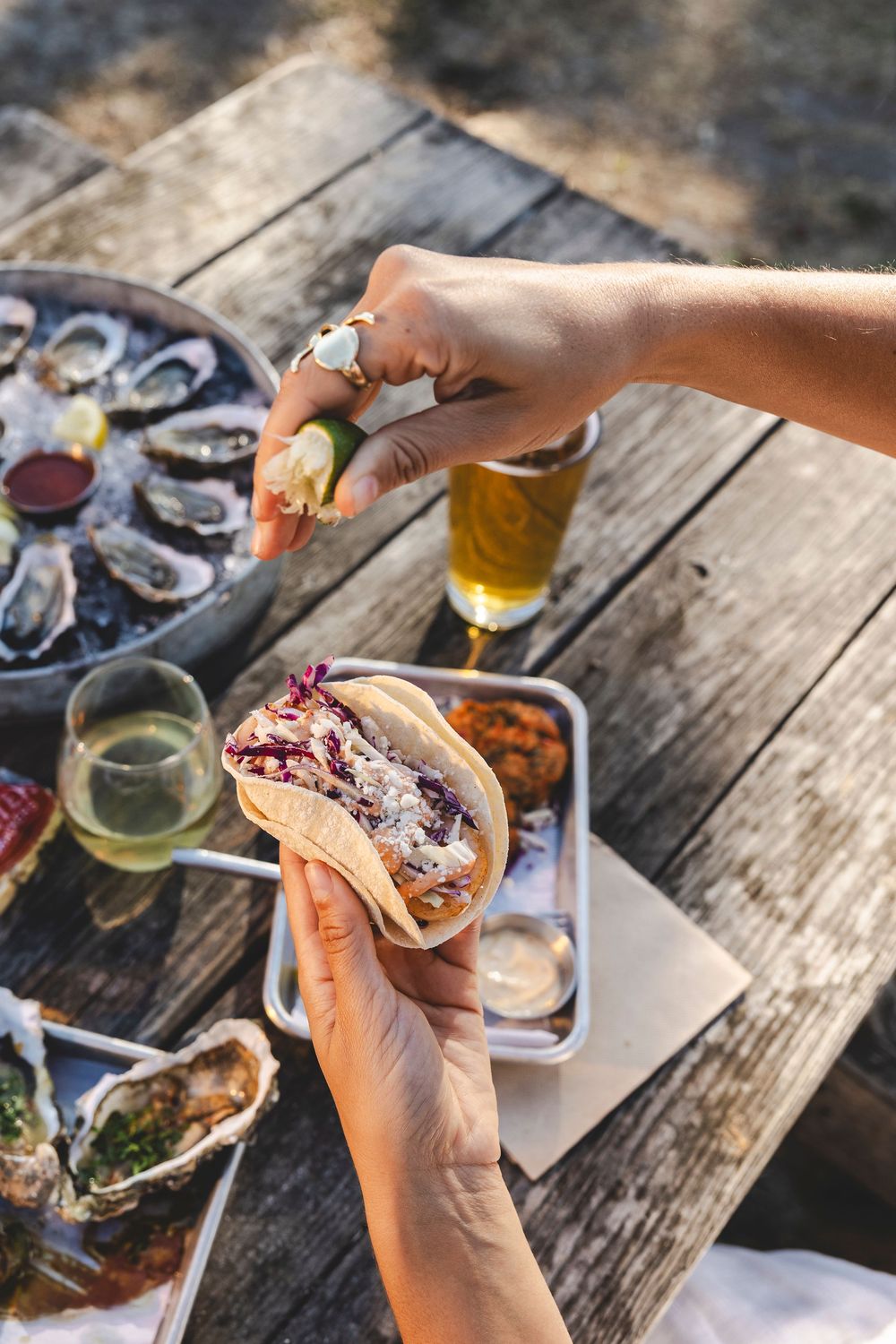 Fresh oysters and craft beers being enjoyed at a rustic wooden table during an outdoor dining experience.