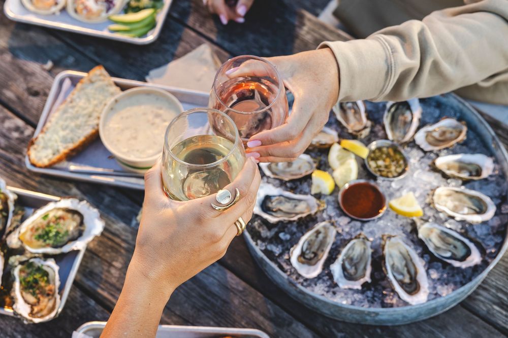 A platter of fresh oysters on ice being served with various sauces and condiments at a restaurant table.