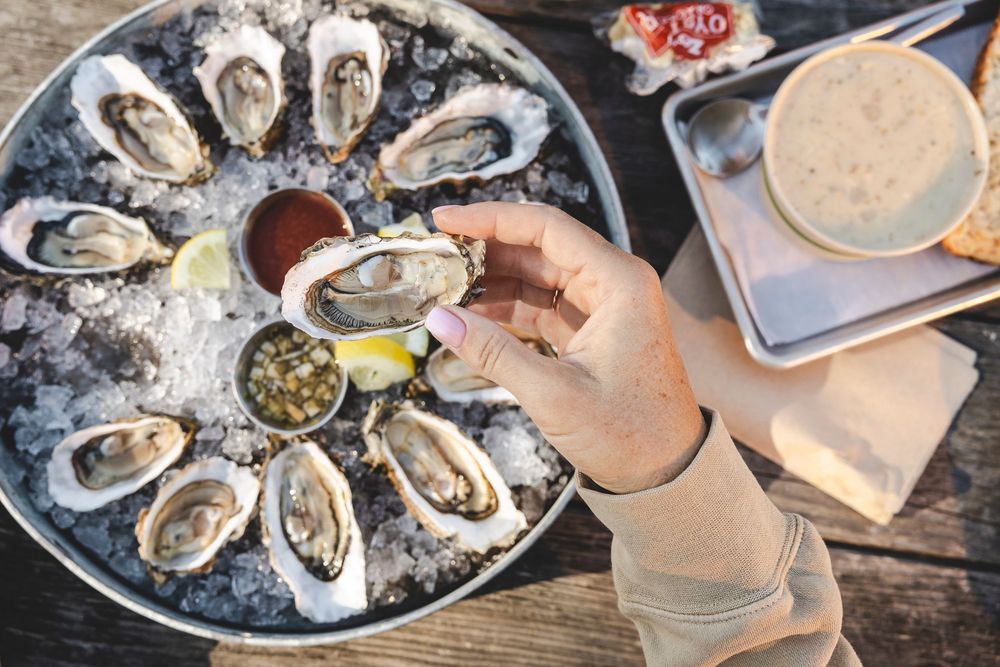 Fresh oysters on ice served with mignonette sauce and lemon wedges on a rustic wooden table.