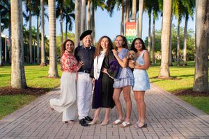 Family of five with a small dog poses together on a palm-lined University of Miami walkway.