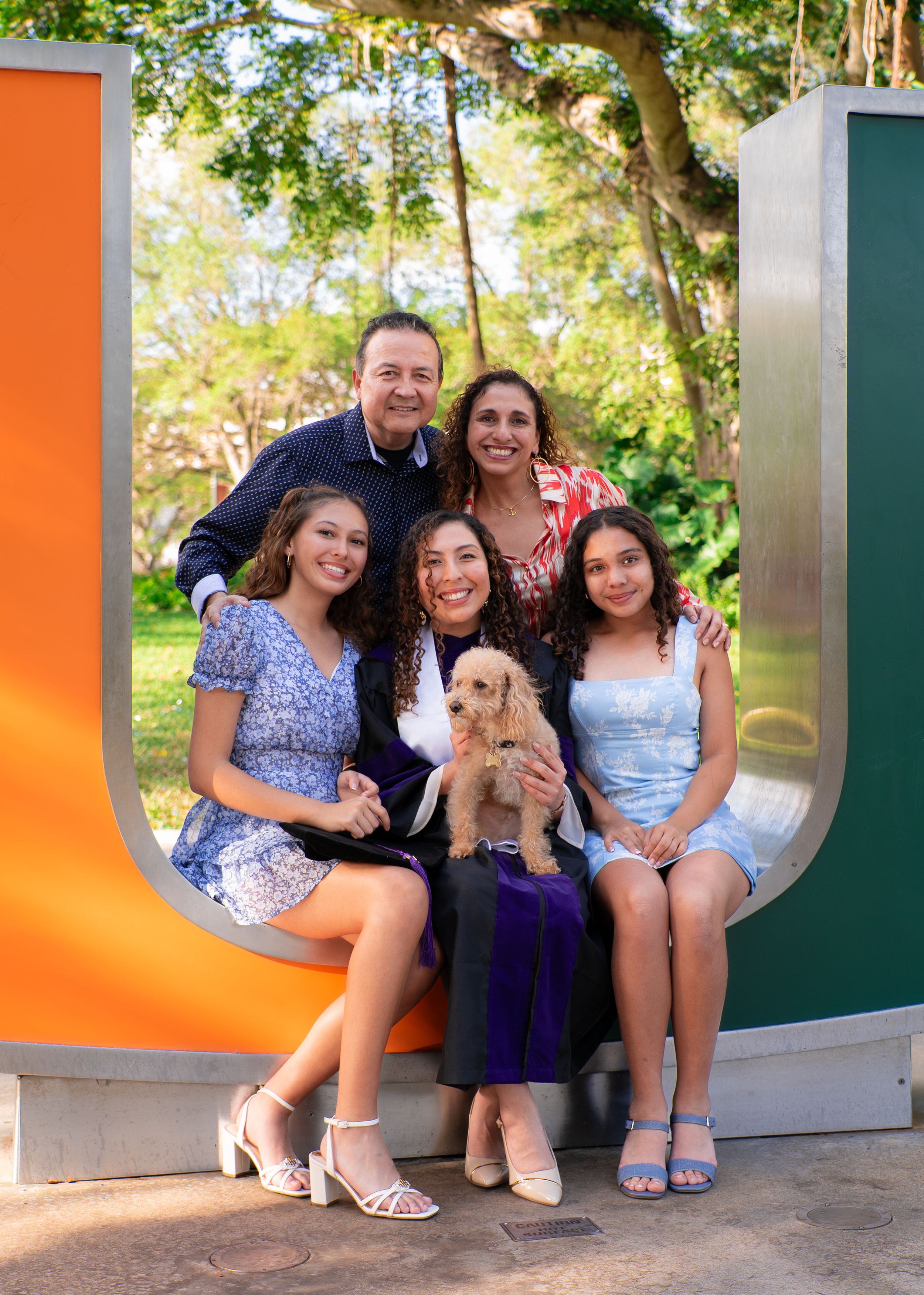 Happy family of five with a puppy poses together at the University of Miami U sculpture.
