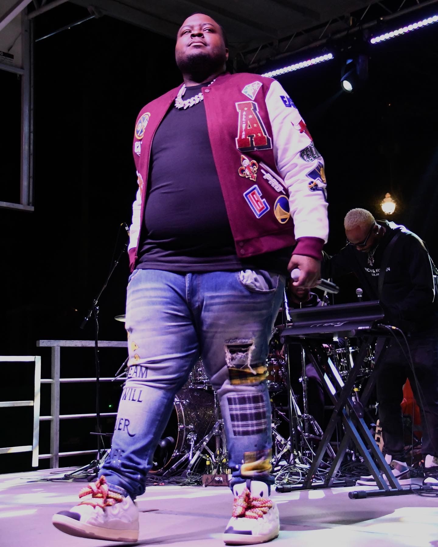 A performer in a purple shirt and light colored pants stands on stage with dramatic lighting effects.