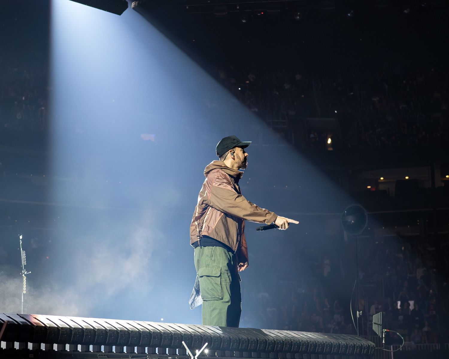 Dramatic concert stage lighting illuminates a performer silhouetted against a smoky blue backdrop during a live show.