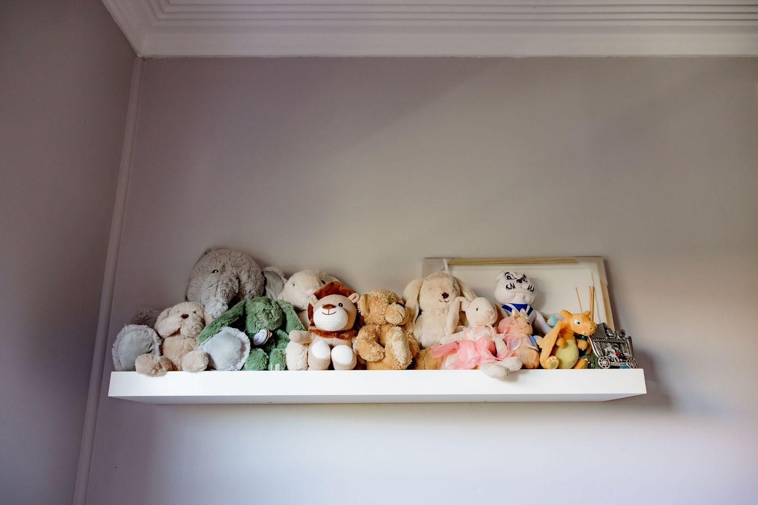 A collection of plush stuffed animals neatly arranged on a white floating shelf against a gray wall.