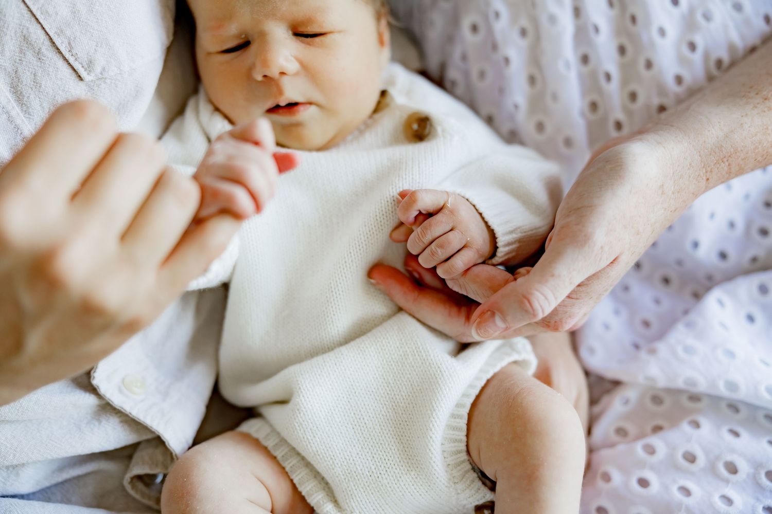 Small baby wearing white clothing rests on polka dot bedding while being cared for by adult hands.